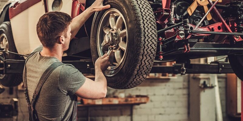 Mechanic working on classic car wheels and suspension in restora
