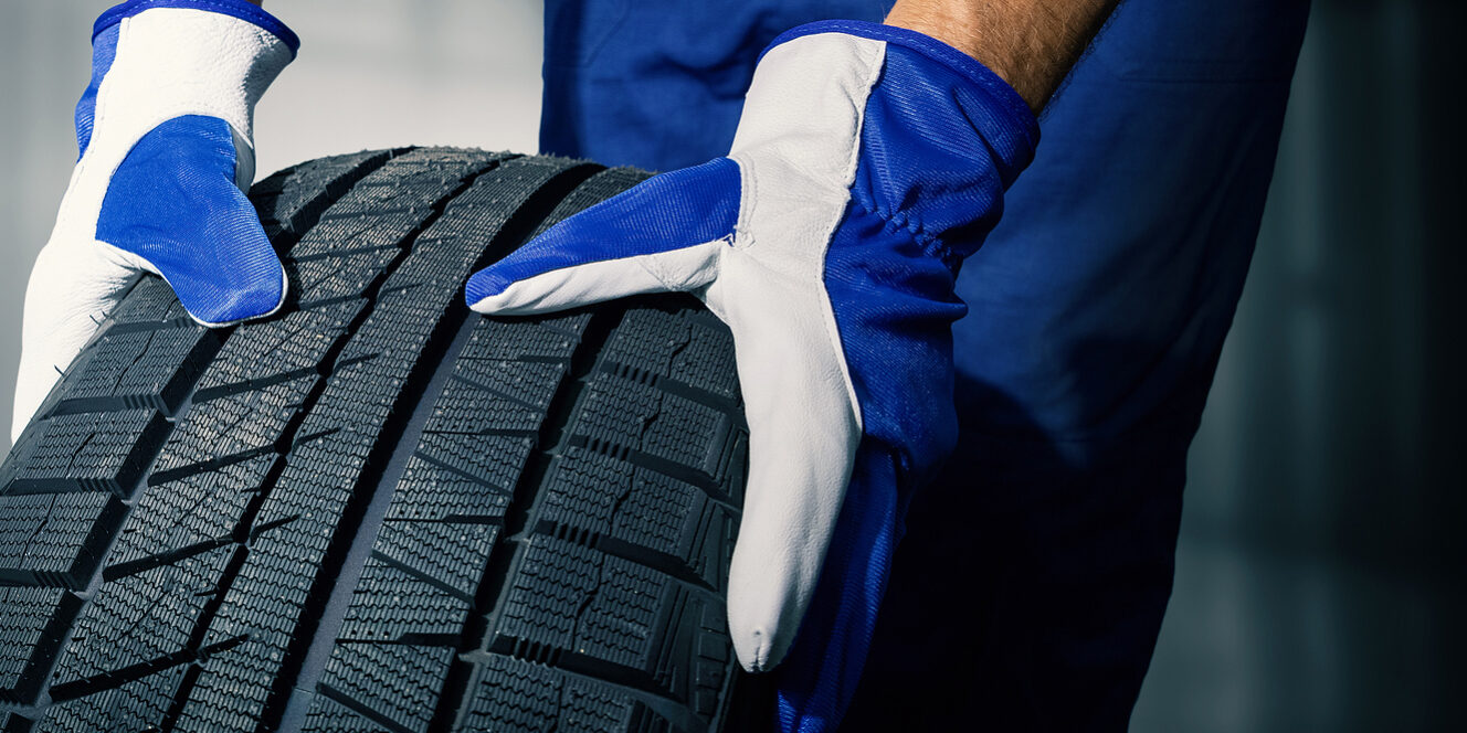 Car Tire Shop And Service – Mechanic Holding New Tyre On Garage