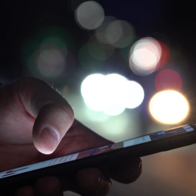 Hand Of A Man With A Smartphone In The City At Night Against The