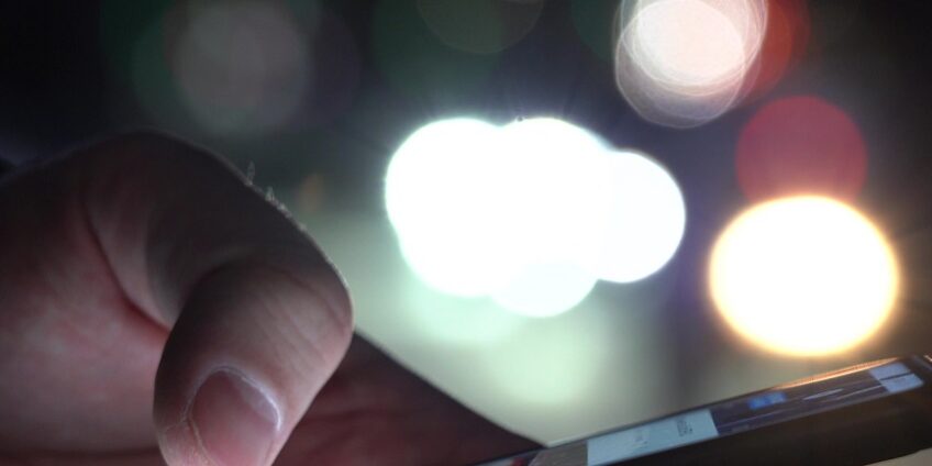 Hand Of A Man With A Smartphone In The City At Night Against The