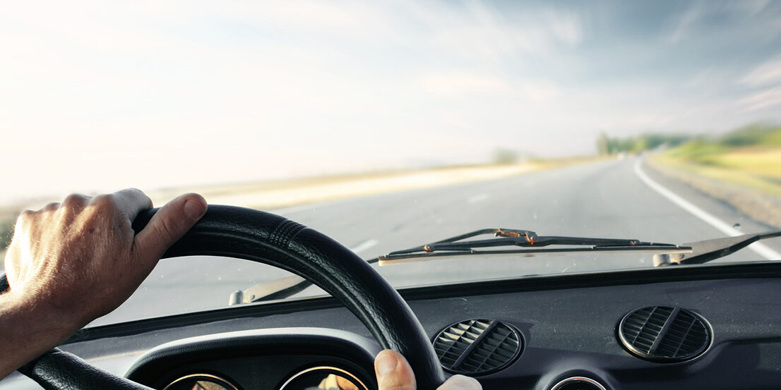 Driver’s hands on a steering wheel of a car and blue sky with bl
